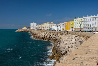 Buildings by sea against blue sky