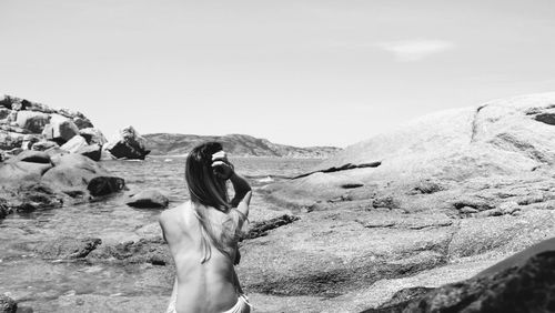 Rear view of woman sitting on rock against sky