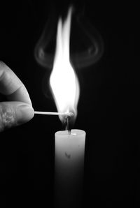 Close-up of cropped hand lighting matchstick from candle against black background