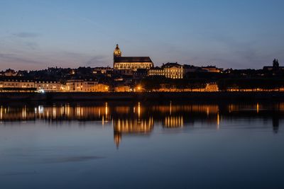 Illuminated buildings by river against sky at night