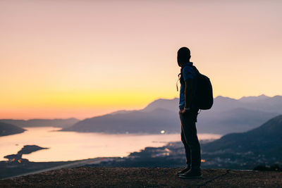 Side view of man standing on mountain against sky during sunset