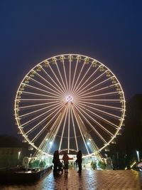People in illuminated ferris wheel against sky at night
