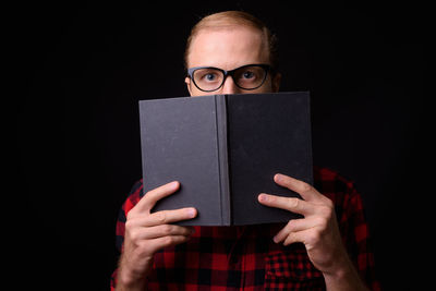 Portrait of man reading book against black background