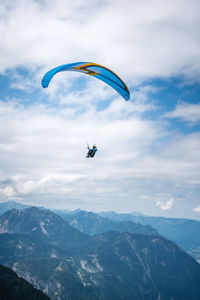 Person paragliding over mountains against sky