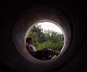 Side view of woman sitting in tunnel against trees