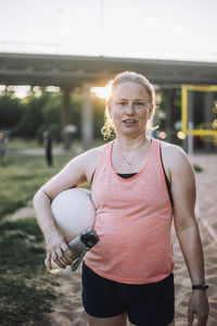 Portrait of woman holding water bottle and volleyball under arm