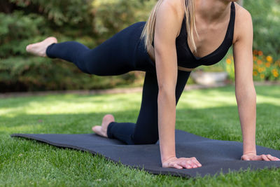 Close up cropped view of young woman in yoga pose while exercising outdoor in black mat over grass
