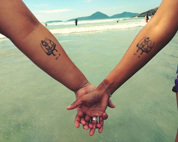 Cropped image of friends with tattoos holding hands at beach