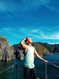 Man standing on boat in sea against blue sky