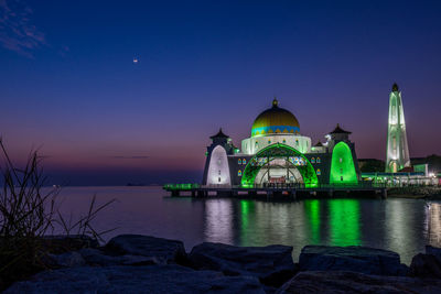 Illuminated building by sea against blue sky during sunset