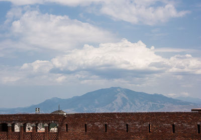 Historical building with mountain range in background against cloudy sky