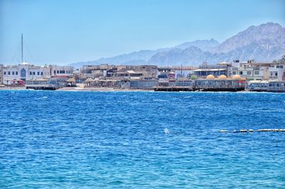 Sailboats in sea by buildings against blue sky