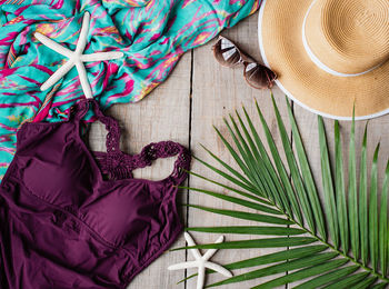 Top view of woman's swimsuit and beach accessories on wood background.