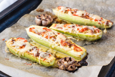 Ready-to-eat baked zucchini halves stuffed with cheese and tomato on baking paper on a baking sheet