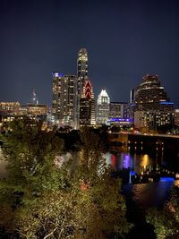 Illuminated buildings by river against sky at night