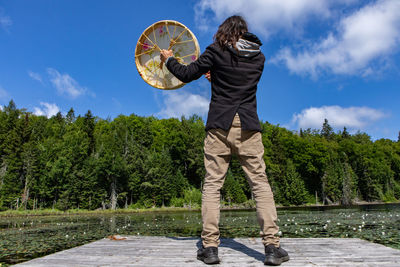 Man holding umbrella standing by plants against sky