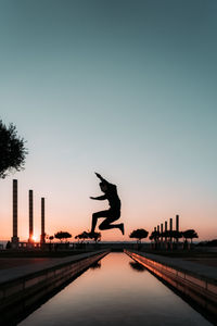 Silhouette man in mid-air against clear sky during sunset