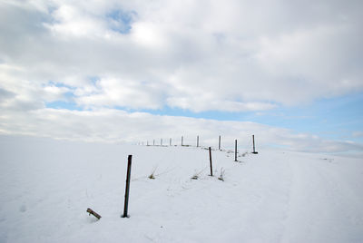 Wooden posts on snow covered field against sky