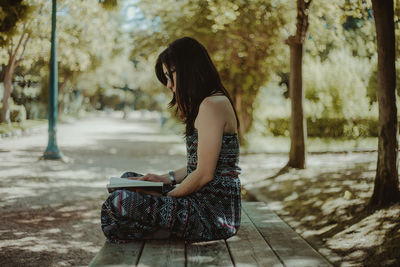 Woman reading book sitting on bench at park