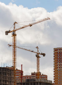 Low angle view of crane by building against sky