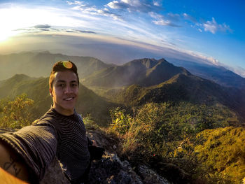 Portrait of smiling young woman standing on mountain against sky