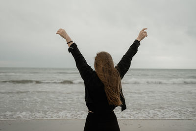 Rear view of woman standing at beach against sky