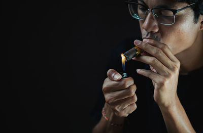 Close-up of man smoking electronic cigarette against black background