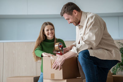 Happy young family couple man and woman packing cardboard boxes together moving in new apartment.