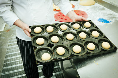 Midsection of chef holding raw cookies in baking sheet