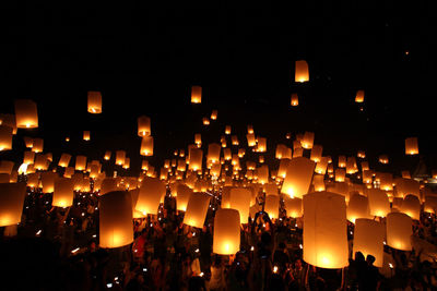 People with illuminated lanterns against sky at night