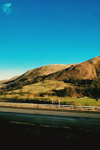 Scenic view of road by mountains against clear blue sky