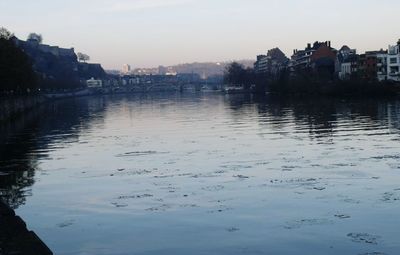 Scenic view of river by cityscape against sky