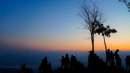 Silhouette people standing by tree against sky during sunset