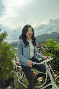 Portrait of young woman sitting on bicycle against sky