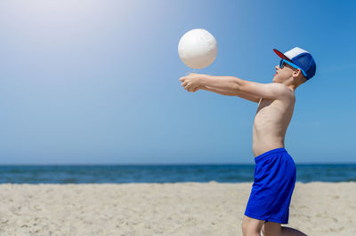 Young man with ball on beach against blue sky