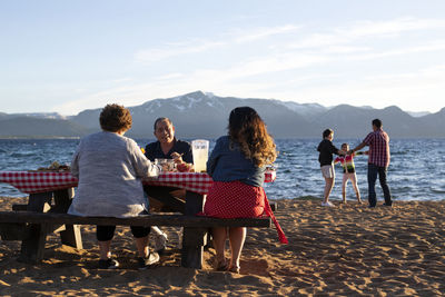 Group of people sitting on shore against mountain range
