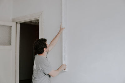 Young caucasian plasterer holds a long spatula and checks the walls for evenness after puttying