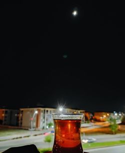 Close-up of beer glass on table against illuminated city at night