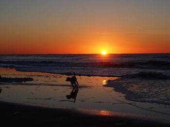 Silhouette man on beach against sky during sunset