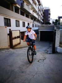 Boy riding bicycle on street against buildings in city