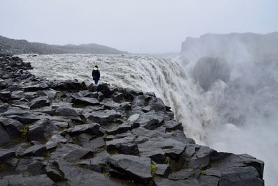 Man standing on rocks by sea against sky