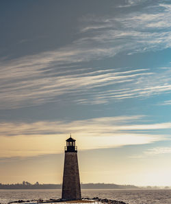 Lighthouse by sea against sky during sunset