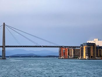Suspension bridge over sea against sky in city