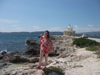 Woman standing on rock by sea against sky