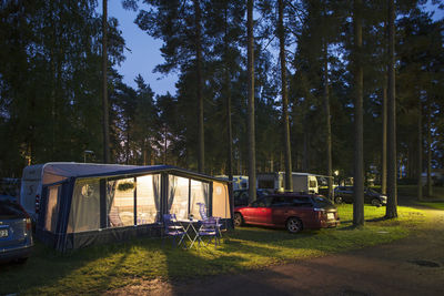 Illuminated tent by caravans in travel trailer park amidst trees at dusk