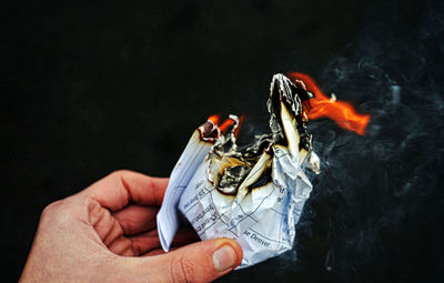 Cropped hand holding burning paper against black background