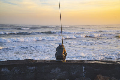 Man fishing on beach against sky during sunset