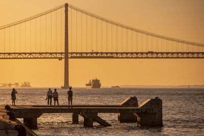 Silhouette people walking on bridge against sky during sunset