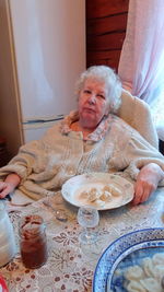 Portrait of senior woman with dumplings sitting by table at home