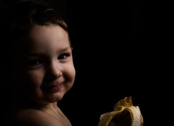 Close-up portrait boy eating banana in darkroom